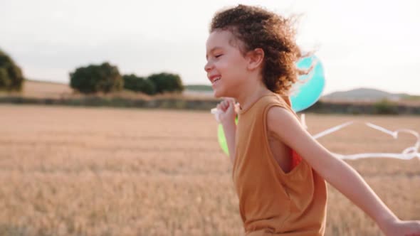 Track shot of happy boy running over countryside field and holding balloons