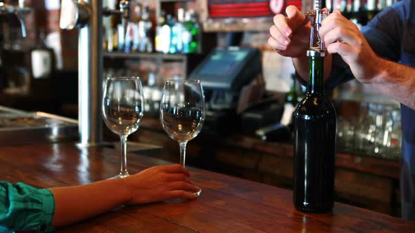 Barman opening wine bottle with corkscrew at bar counter