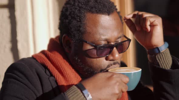 Concentrated African man in eyeglasses drinking coffee in cafe