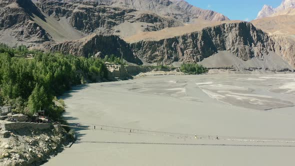 Aerial drone flying backwards as tourists cross the famous Hussaini bridge in Hunza Pakistan with a
