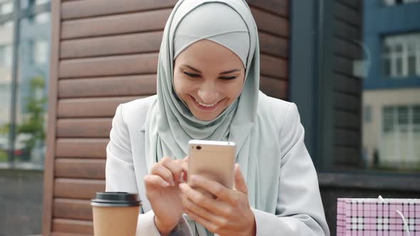 Slow Motion of Cute Arab Woman in Hijab Using Smartphone and Drinking Coffee in Street Cafe