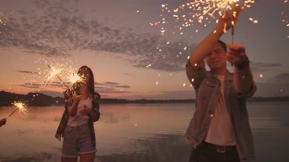 A Group of Friends of Men and Women Merry Celebrate the Holiday on the Beach with Sparklers and