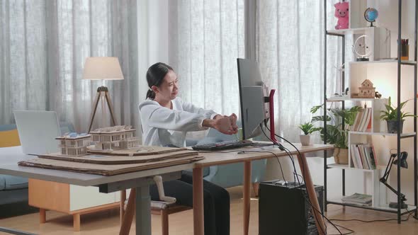 Asian Woman Engineer With The House Model Stretching After Working On A Desktop At Home