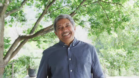 Portrait of happy senior man in blue shirt is standing against trees