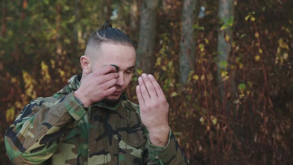 The Soldier in Camouflage Smears Soot on Face at a Forest