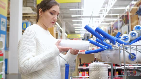 Young Woman Chooses New Painting Roller in Hardware Store