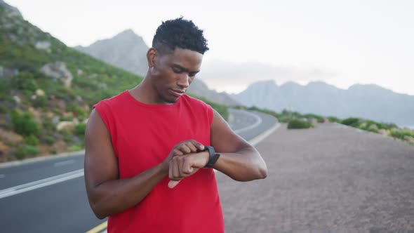 African american man using fitness band while standing on the road