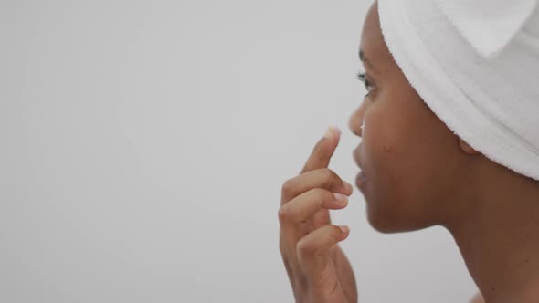 Happy african american woman apply cream on face in bathroom