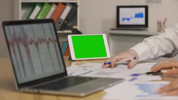 Man and Woman Viewing Papers with Charts and Graphs Using Laptop