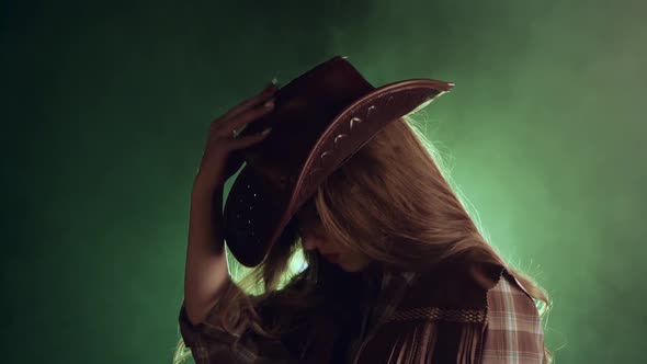 Girl in a Cowboy's Clothes Is Dressing a Hat. Black Smoke Background. Slow Motion
