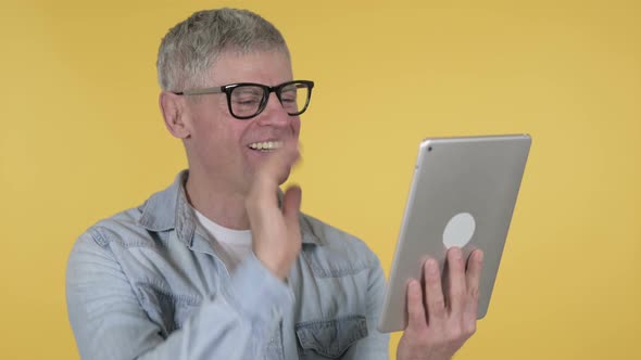 Video Chat By Casual Senior Man Via Tablet Isolated on Yellow Background