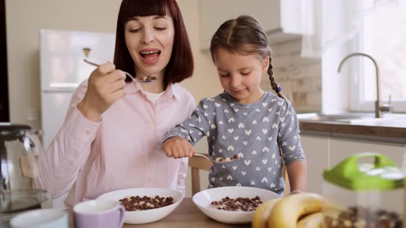 Young Beautiful Caucasian Mother and Her Cute Little Girl Having Breakfast with Chocolate Corn Balls