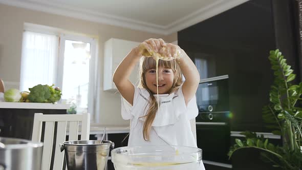 Cute Little Girl with Long Hair in White Dress Kneading the Dough in Glass Bowl