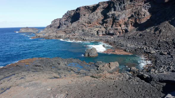 Aerial dolly from fishing village over ocean coast and hardened lava