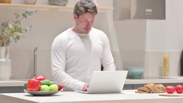 Middle Aged Man Working on Laptop in Kitchen