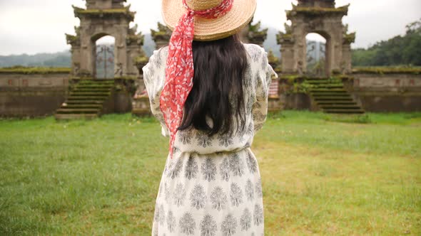 Young Mixed Race Traveler Girl in Straw Hat and Ornament Dress Taking Photo of Balinese Temple