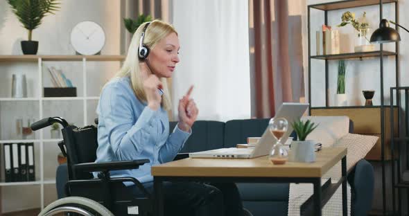 Female Coach in Headphones which Sitting in Wheelchair at Home and Holding Online Webinar