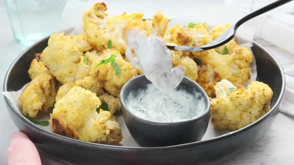 Baked spicy cauliflower with yogurt sauce in black plate.