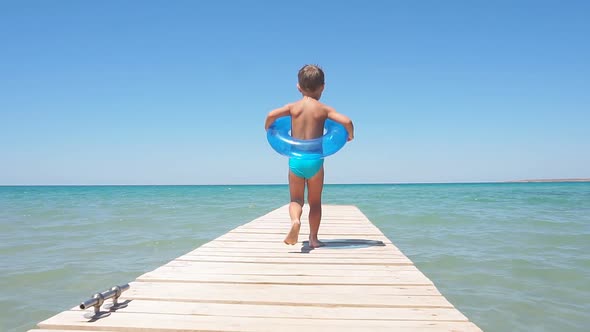 Happy Boy or Child Running Along the Pier Towards the Azure Sea, Slow Motion. Sunny Warm Day in