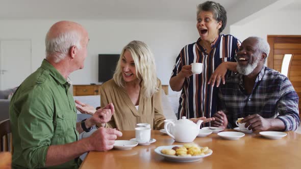 Two diverse senior couples sitting by a table drinking tea together at home