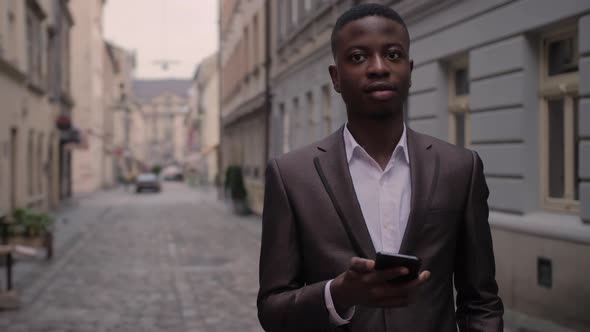 African Man in Suit Standing on Street with Smartphone