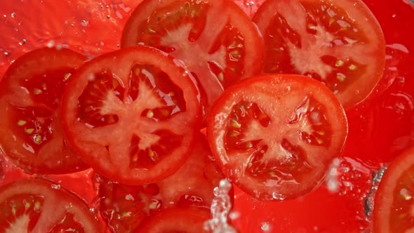 Super Slow Motion Shot of Tomato Slices Falling Into Water on Red Background at 1000Fps.