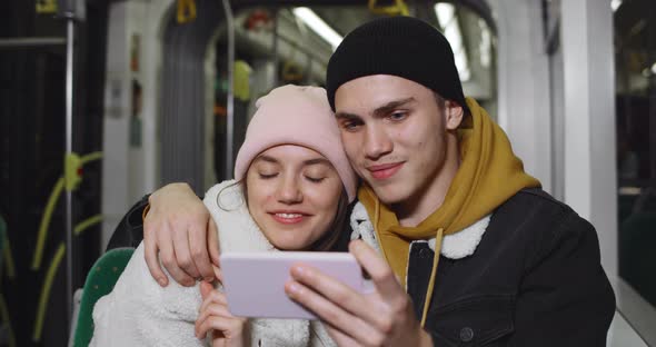 Millennial Couple Watching Funny Video on Smartphone and Laughing While Sitting Together in Bus