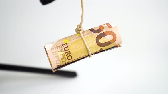 Rolled fifty euro bills hang from a money rubber band and swing against a white background