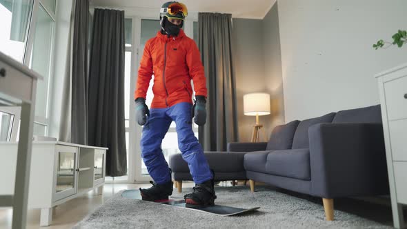 Fun Video. Man Dressed As a Snowboarder Rides a Snowboard on a Carpet in a Cozy Room. Waiting for a