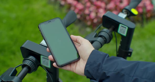 Young Man Paying For Electric Scooter Use App with Green Mock-up Screen Smartphone. Green Screen