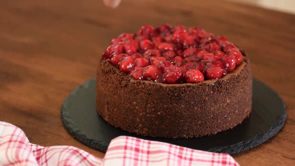 Woman decorates chocolate cheesecake with cherry sauce