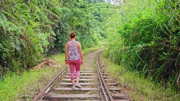 4K Parallax of Caucasian woman walking in slow motion down the middle of a train track in the jungle
