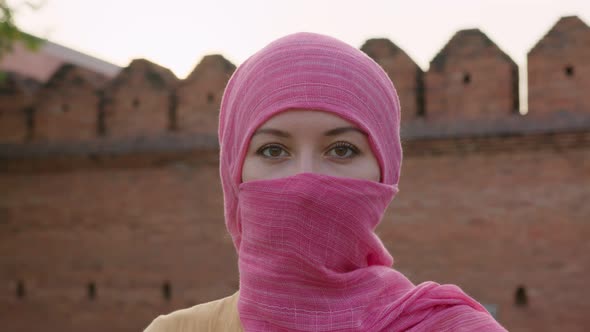 Attractive Muslim Woman with Natural Make Up Wearing Pink Hijab Scarf Looks at Camera