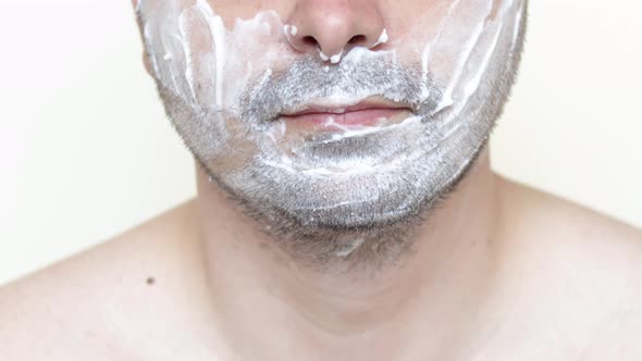 young man with shaving foam on face is smiling.guy using razor to shave beard.feeling pain.daily