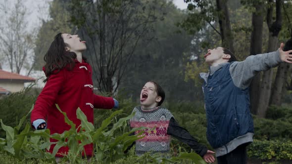 Three kids standing enjoying the pouring rain in slow motion