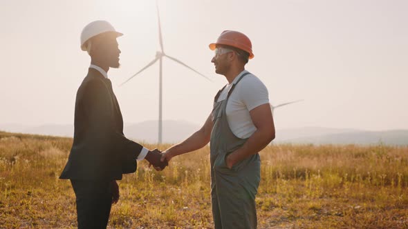 Man in White Helmet and Black Suit Shaking Hands with Indian Engineer with Wind