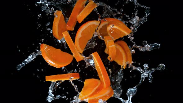 Super Slow Motion Shot of Rotating Exploded Orange Slices with Splashing Water on Black at 1000Fps