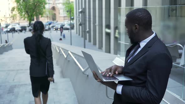 Man Working with Laptop Outside Office Giving Judgmental Look to Female Passerby