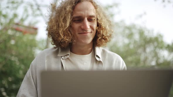 Smiling curly-haired man working on laptop