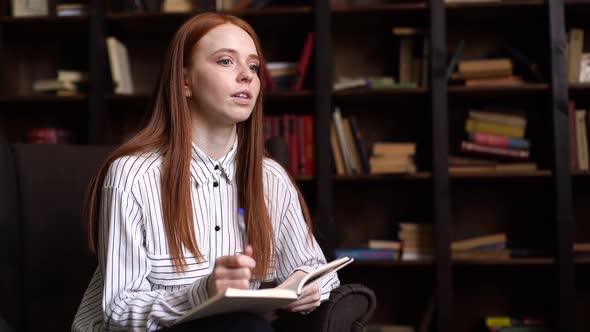 Portrait of Attractive Red-haired Young Woman Journalist Interviewing Person in Cozy Dark Room.