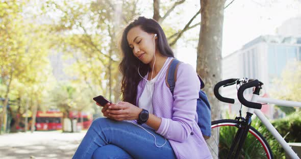 Asian woman wearing earphones using smartphone sitting in the park