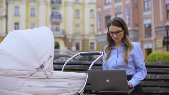 Happy Working Mom With Laptop Swinging Newborn in Carriage, Family and Career