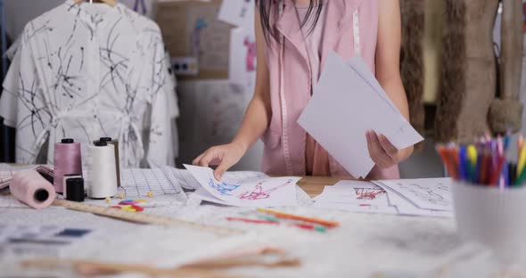 Young Asian fashion designer or stylist choosing sketches for the new dress