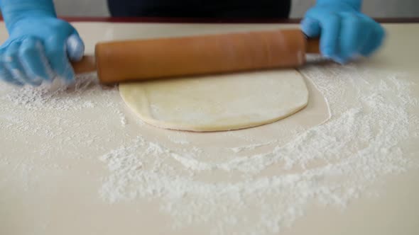 Rolls Out the Dough on the Kitchen Table. Female Hands Rolling Dough with a Rolling Pin, Close Up