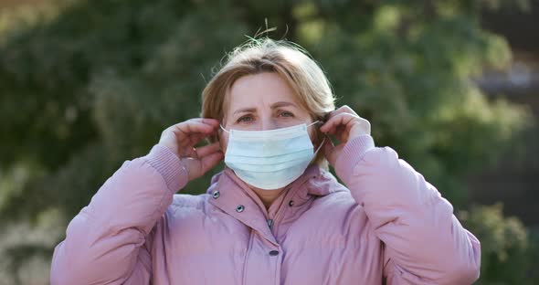 Senior Woman Takes on Medical Mask and Looking at Camera on Green Background