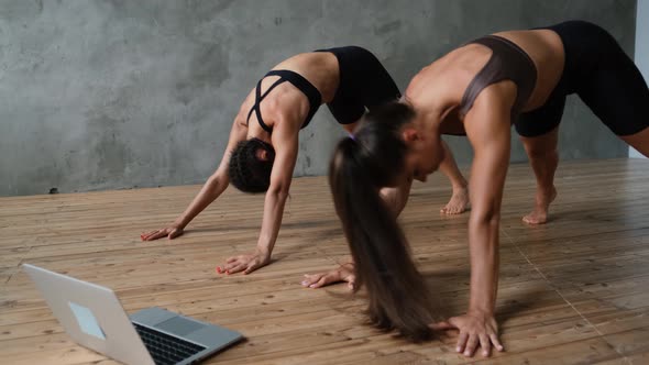 Young Sports Girls Twins are Doing Sports Exercises Indoors at Home Using a Laptop Computer