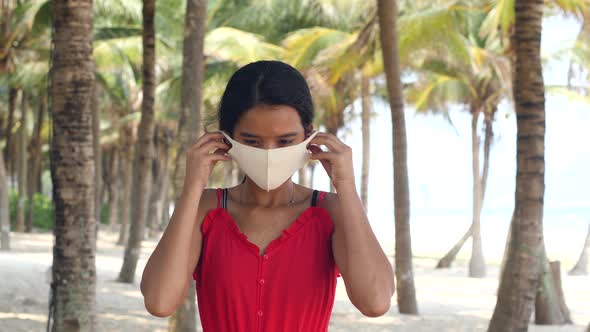 Young Asian Woman Wearing Mask at the Beach, Palm Trees Bakground.
