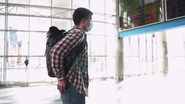 A Man with a Mask Takes Out a Passport and Tickets From His Pocket Watching the Departure Timetable