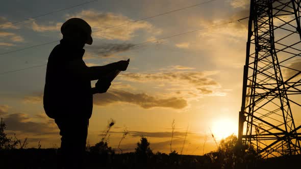 Silhouette of Engineer Standing on Field with Electricity Towers. Electrical Engineer with High