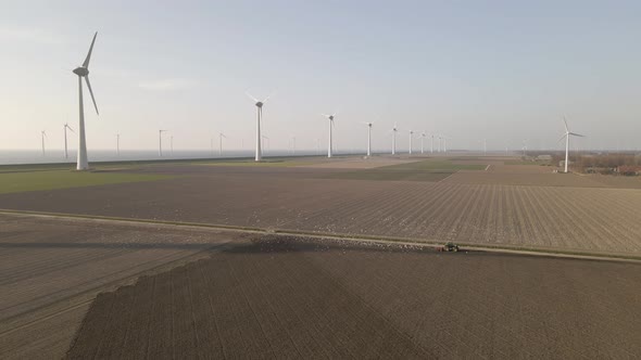 Drone Shot of a Tractor Preparing the Farm Fields on a beautiful day with Windmills in the backgroun